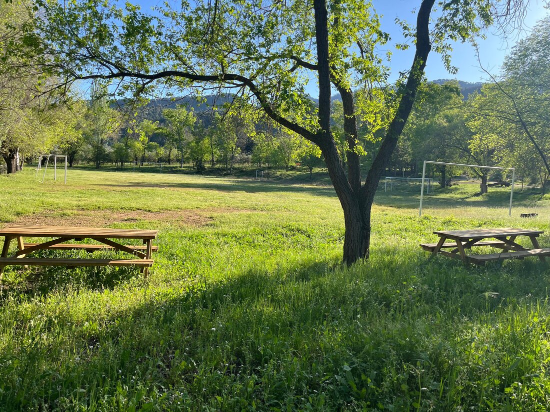 Prado soleado de la finca, con porterías de fútbol y montañas al fondo