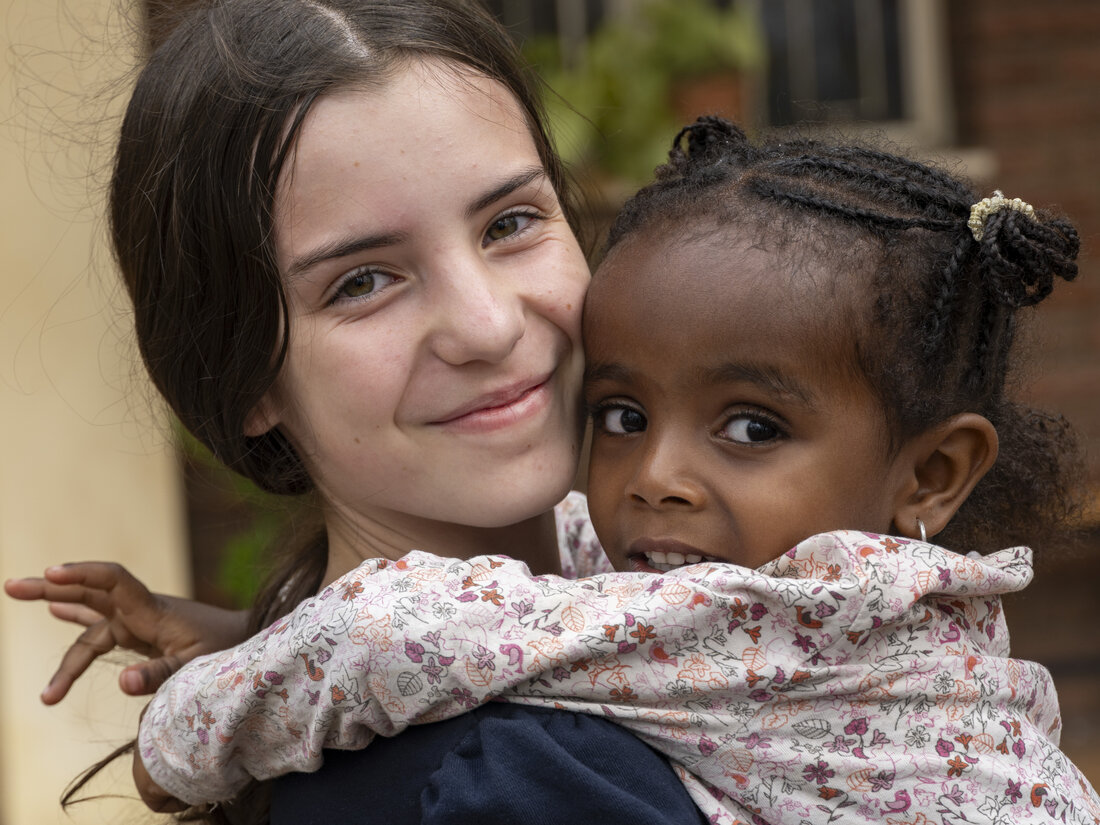Alumnos de ChezNous con niños locales a hombros frente al edificio de la misión
